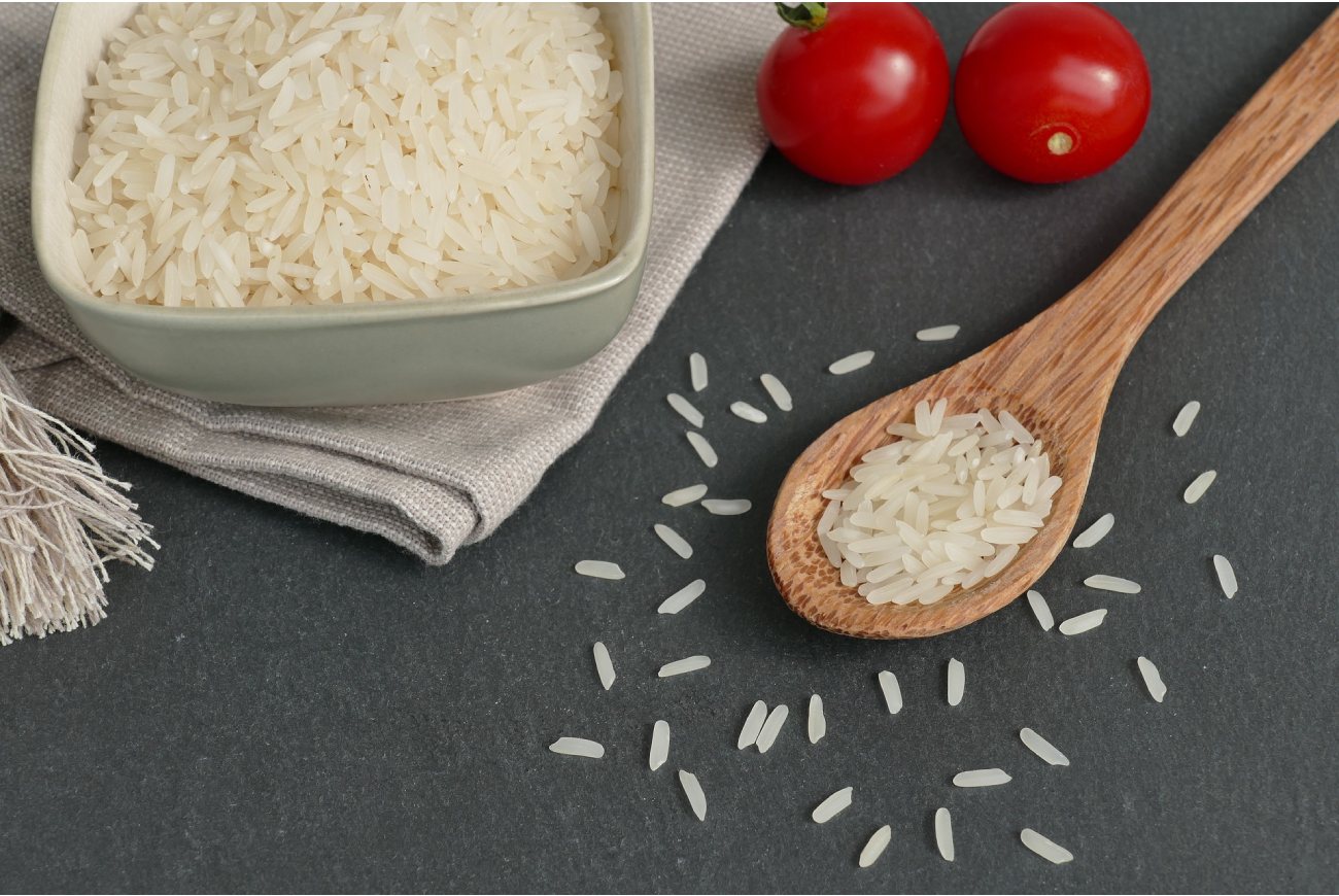 Arroz crudo en un plato y una cuchara con dos tomates crudos