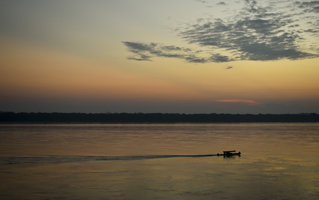 Se ve un barco navegando por el río Amazonas al atardecer.
